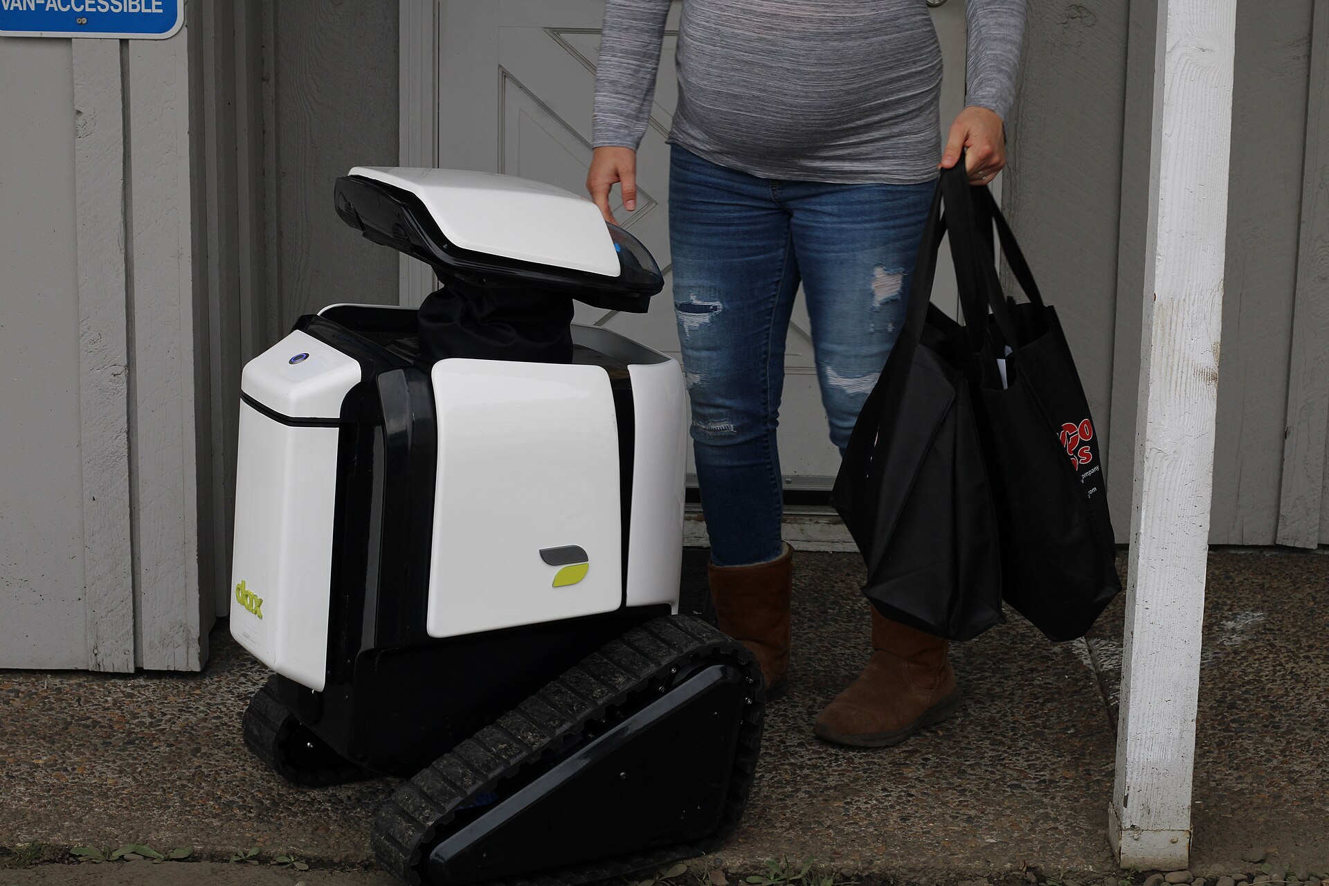 A small delivery robot receiving a bag of groceries