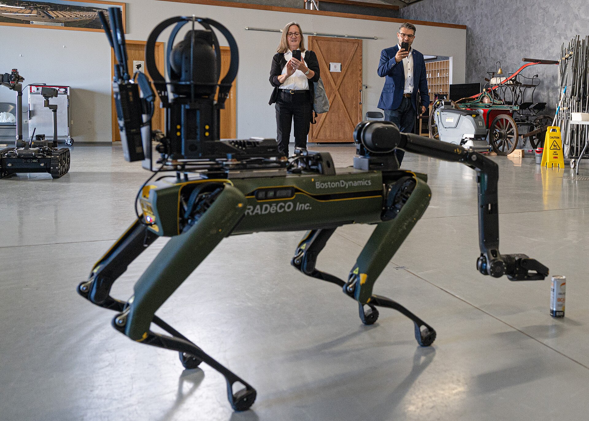 A quadruped robot with an arm walking through a hangar